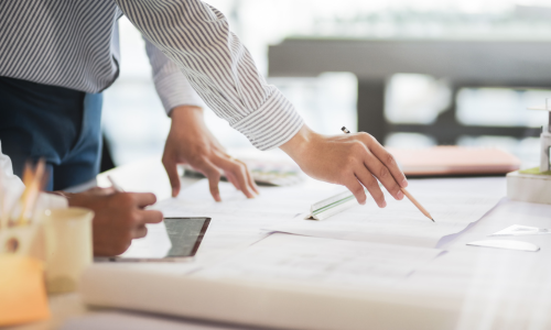 An individual pointing a pencil to a blueprint spread across a table